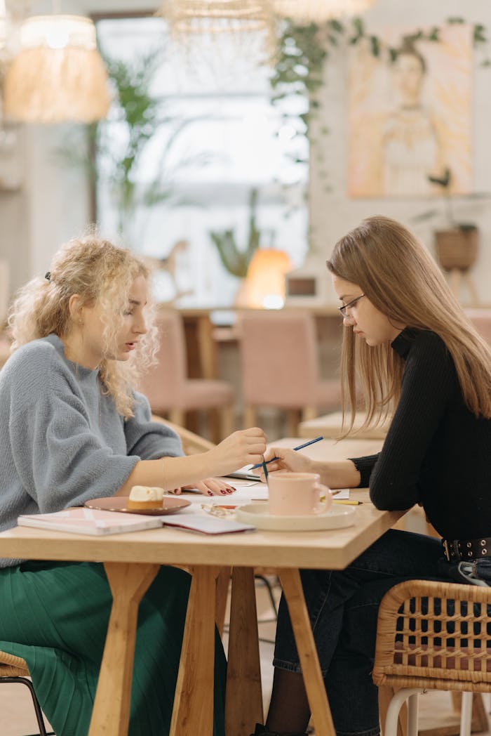 Two young women engaged in serious discussion and planning at a cafe table indoors.